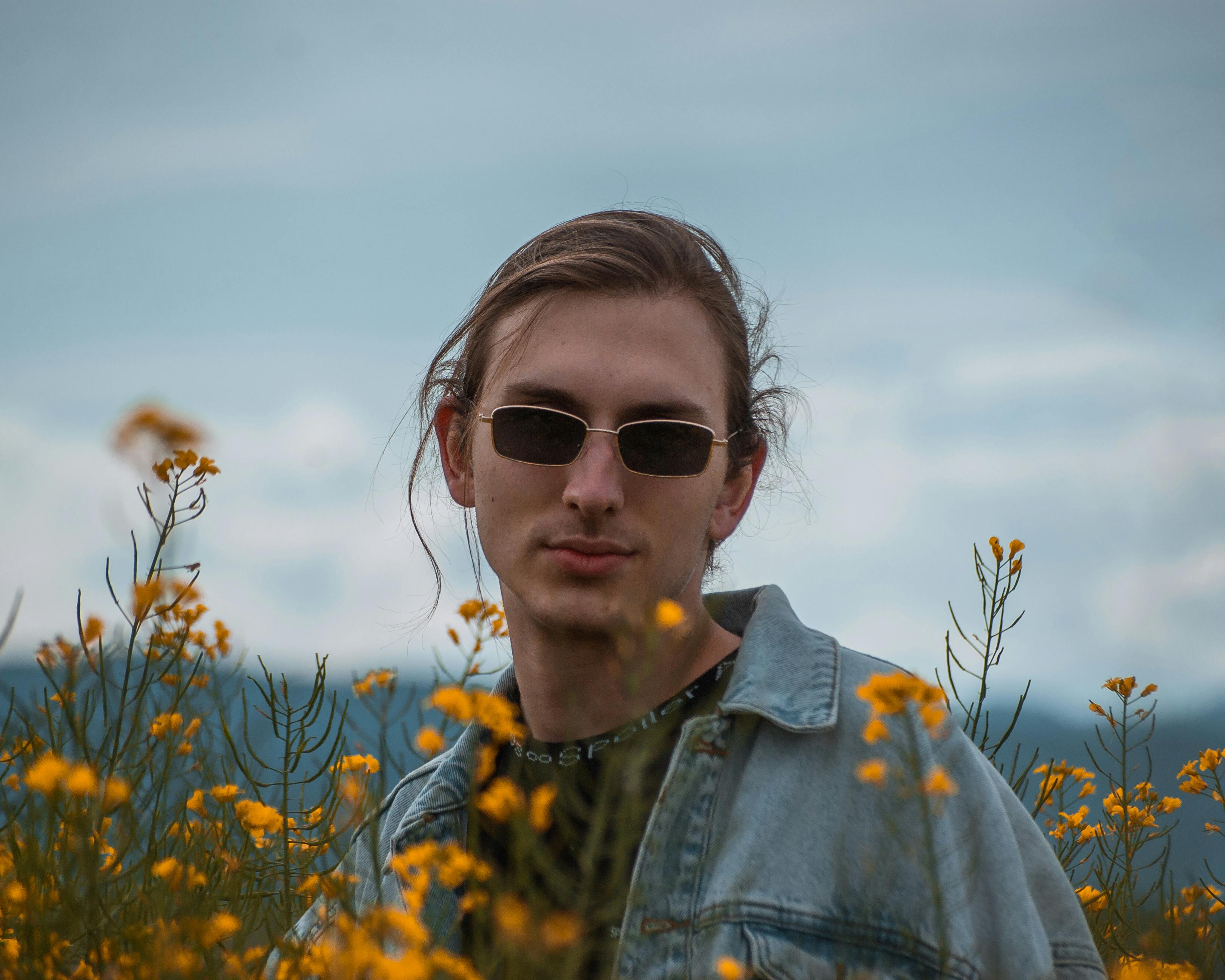 在宁静的田野中，一位戴着墨镜的年轻人被鲜艳的黄色花朵包围