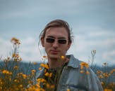 在宁静的田野中，一位戴着墨镜的年轻人被鲜艳的黄色花朵包围