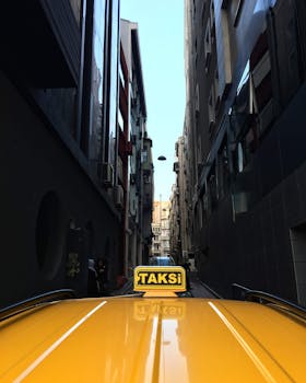 一辆黄色出租车行驶在狭窄的城市小巷中，两旁高楼林立，展现了城市生活