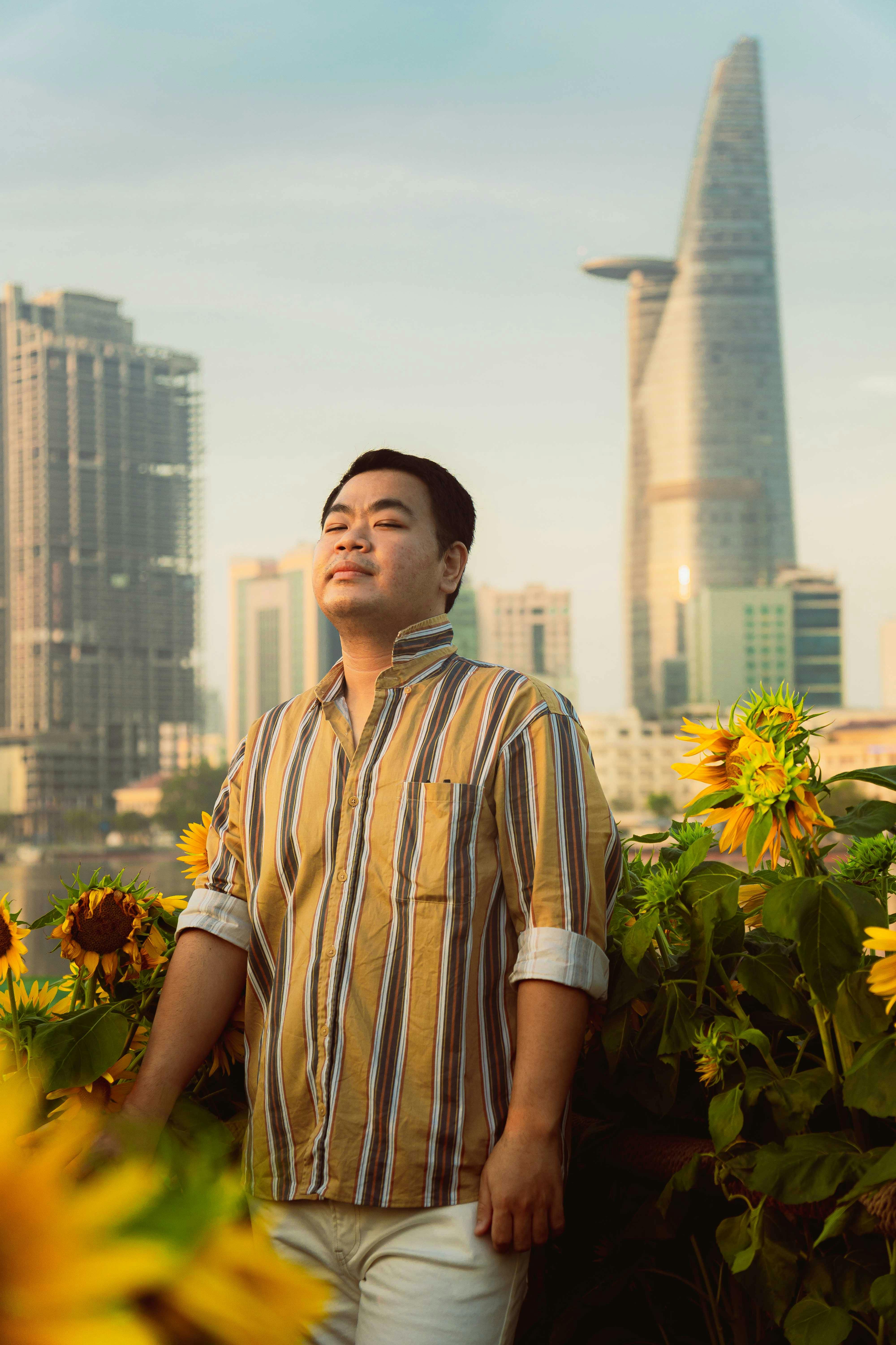Man enjoying sunlight amid vibrant sunflowers with cityscape backdrop in Ho Chi Minh City, Vietnam.
