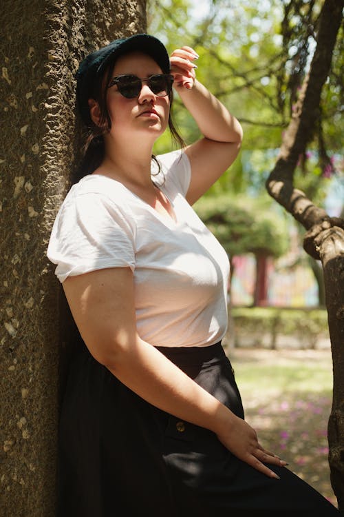 A woman leaning against a tree wearing a white shirt and black skirt
