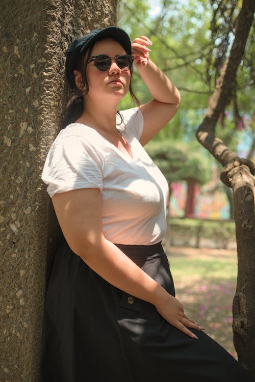 A woman leaning against a tree wearing a white shirt and black skirt