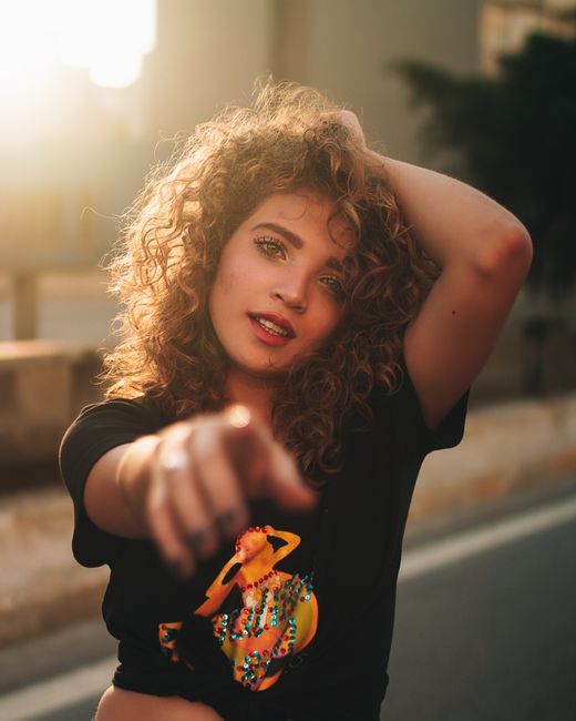 Portrait of a fashionable woman with curly hair posing outdoors in warm sunlight.
