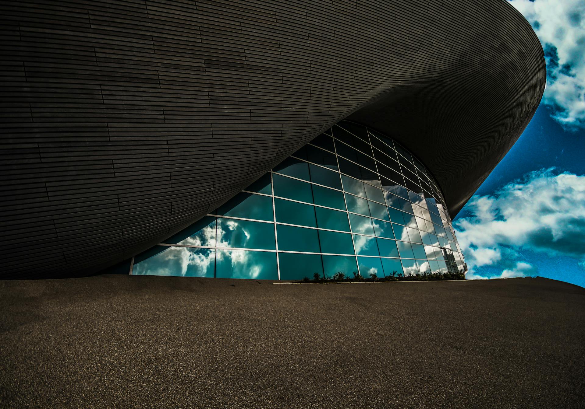 Contemporary architecture with glass panels reflecting a vibrant sky, captured in Olympic Park, London.