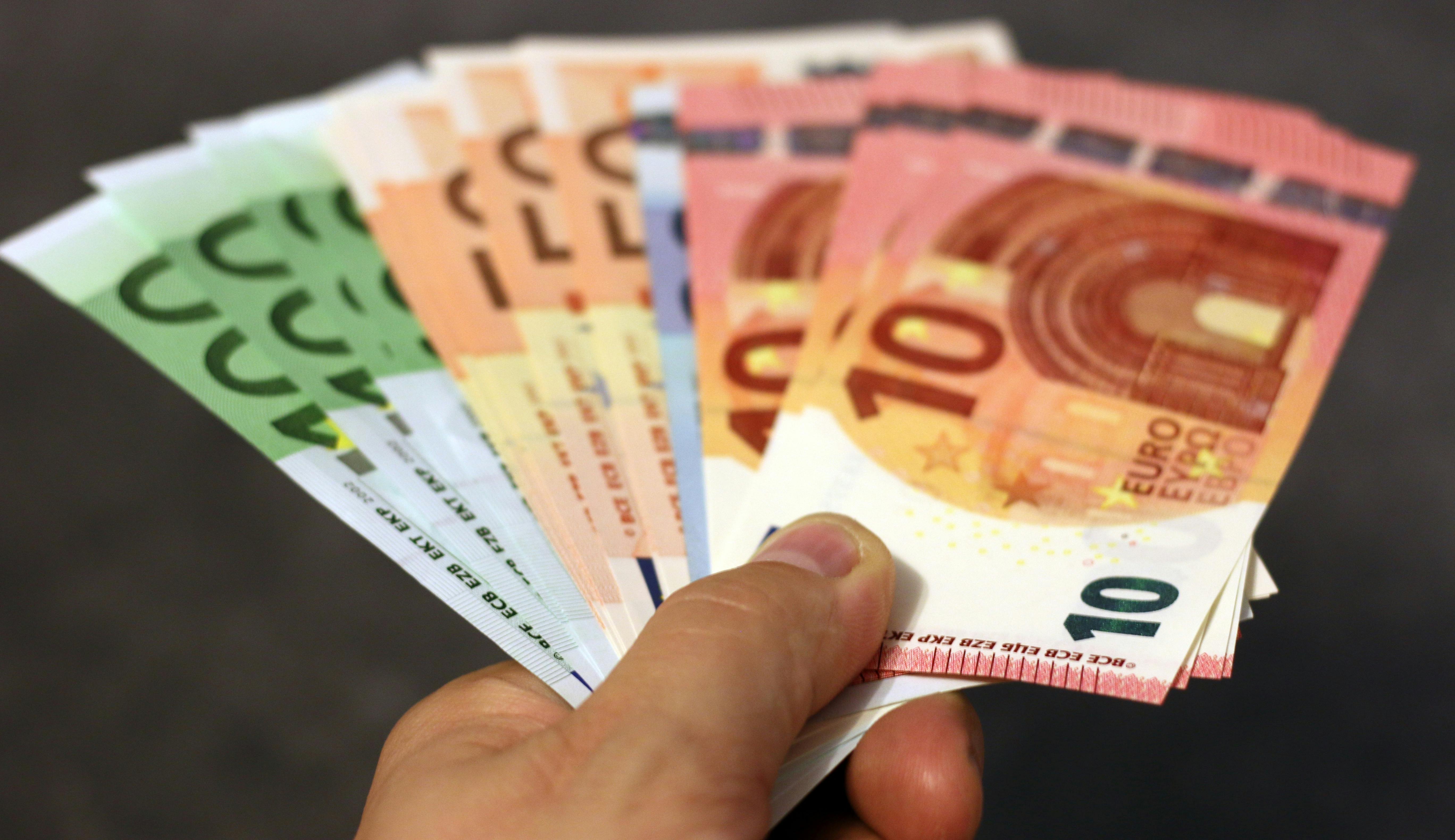 Hand holding fanned euro banknotes, including €10, €20 and €50 notes, against a blurred background