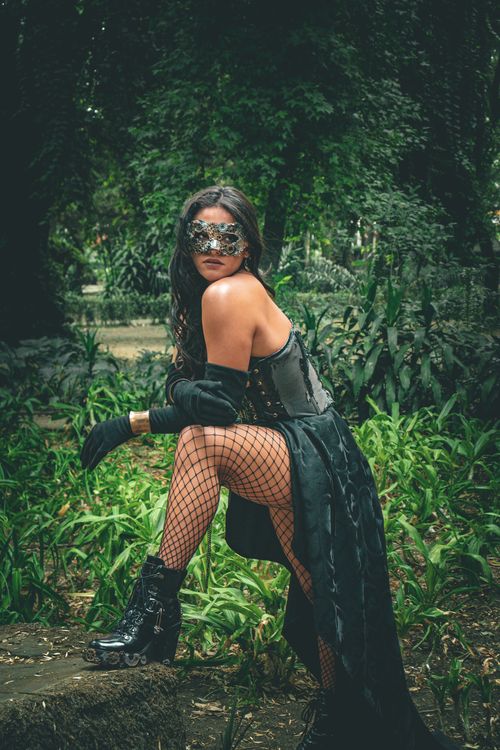 Free A woman poses in steampunk attire amidst a lush garden, embodying mystery and style. Stock Photo