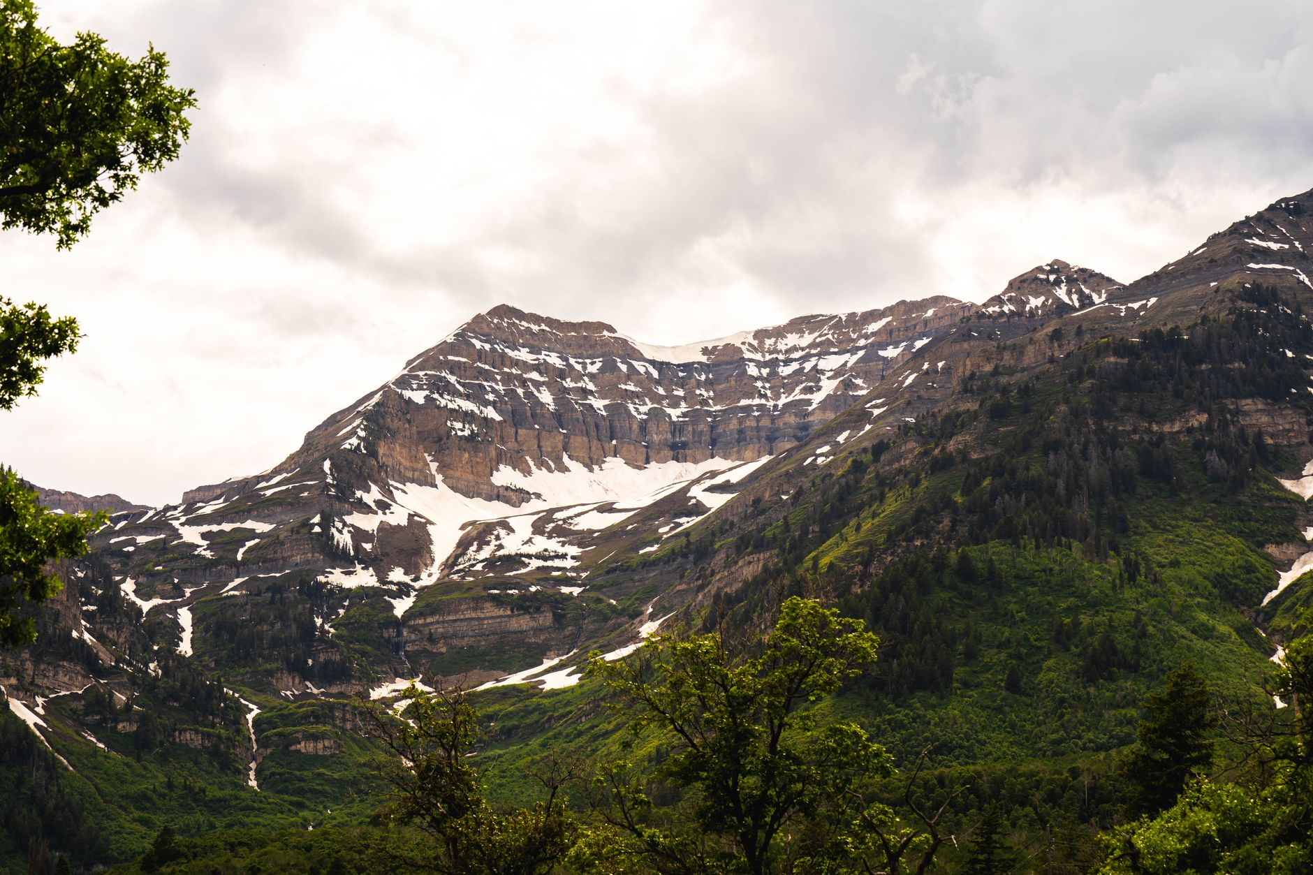 Stunning mountain landscape of the Wasatch Range with snow patches and lush greenery under cloudy skies.