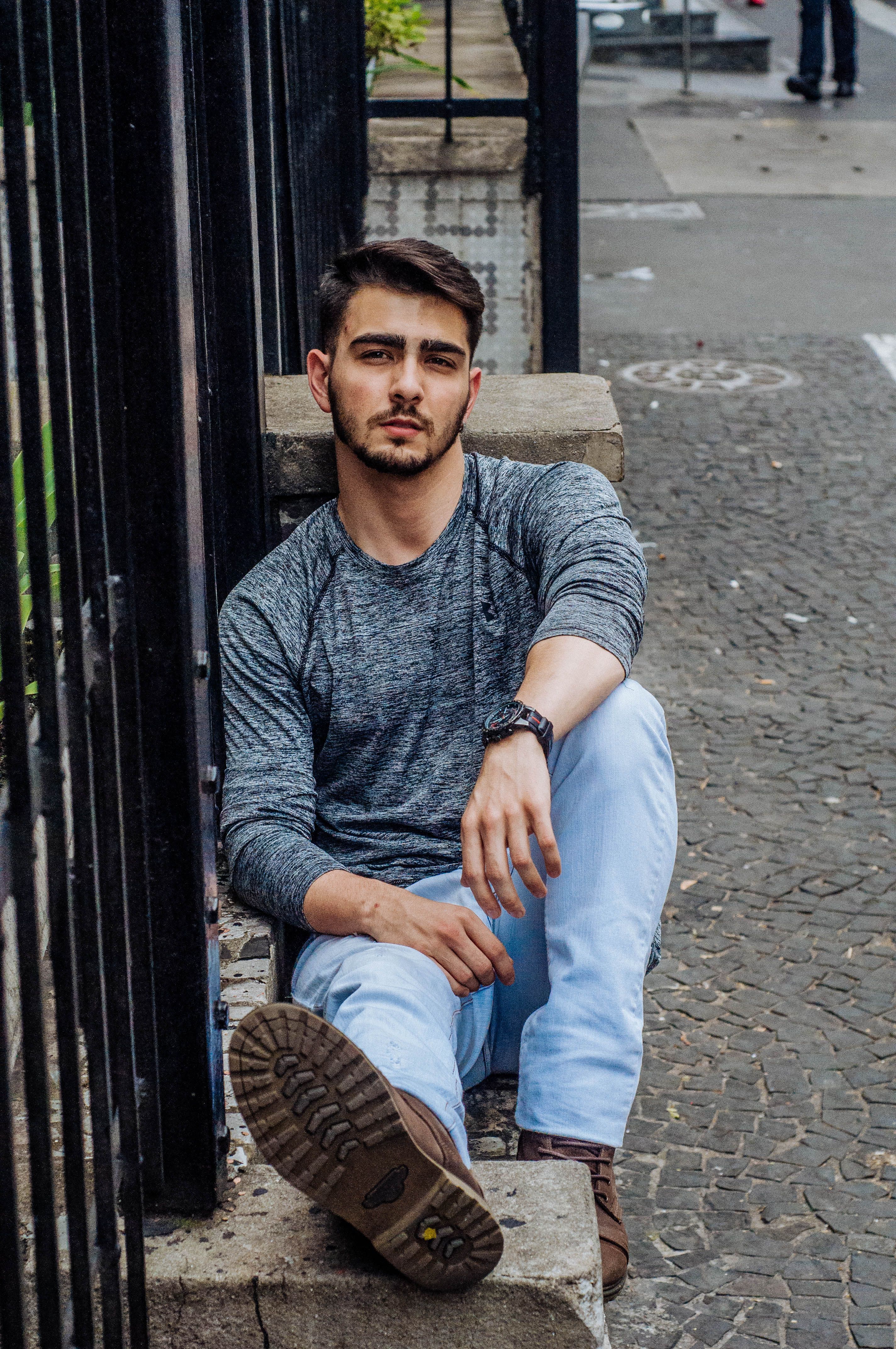 Casual young man sitting on a city street in jeans, exuding modern urban fashion style.