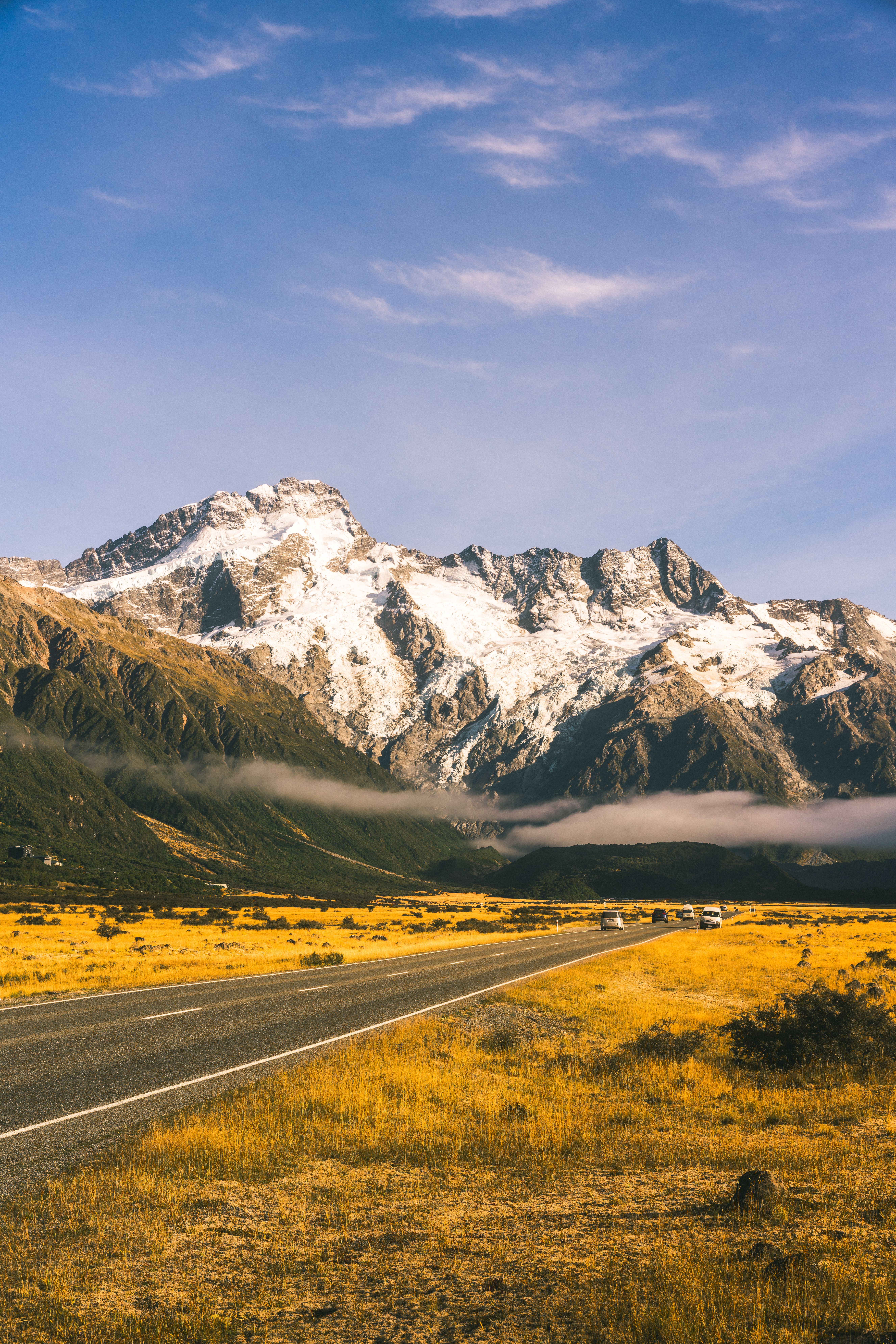 A picturesque road leading to majestic snowcapped mountains under a clear blue sky.