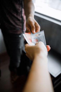 Close-up of hands exchanging Malaysian Ringgit notes indoors.