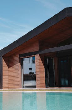 Chic modern house featuring wooden paneling and a pool reflecting the architecture.