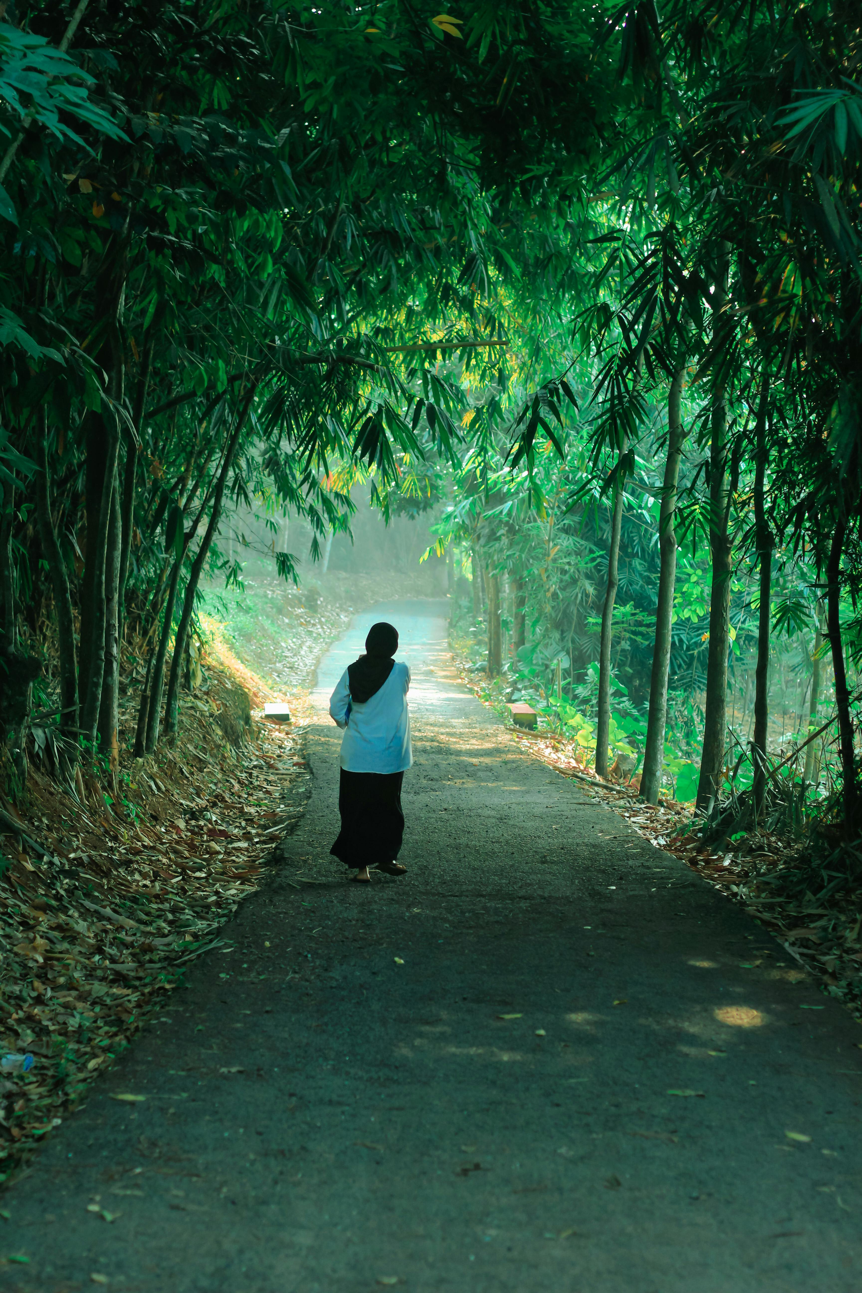 A woman walks down a lush, green forest path in West Java, Indonesia.