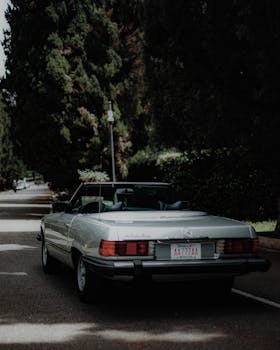 Vintage Mercedes-Benz SL convertible parked on urban street with trees.