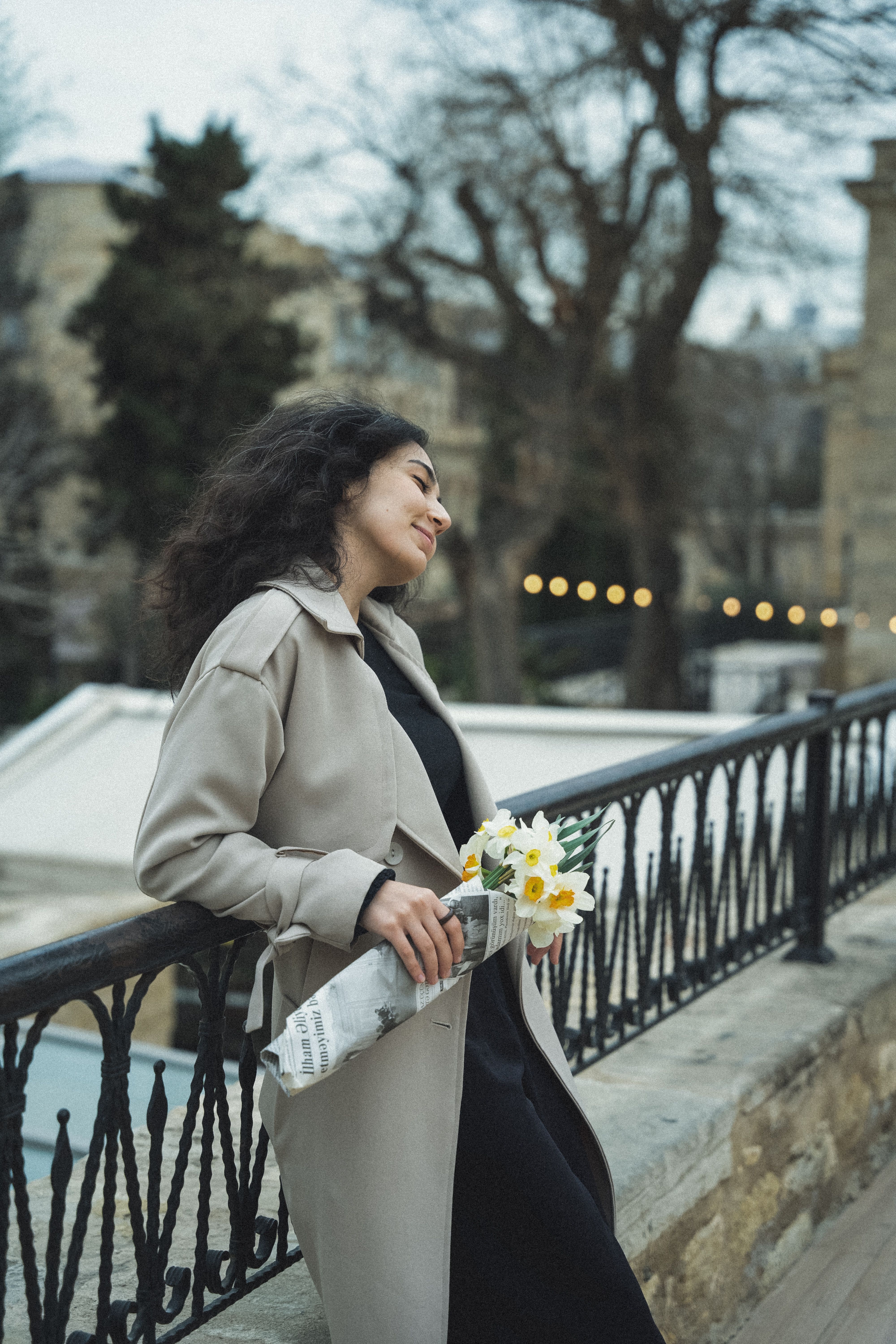 Woman in Baku enjoying a serene moment holding flowers with cityscape backdrop.