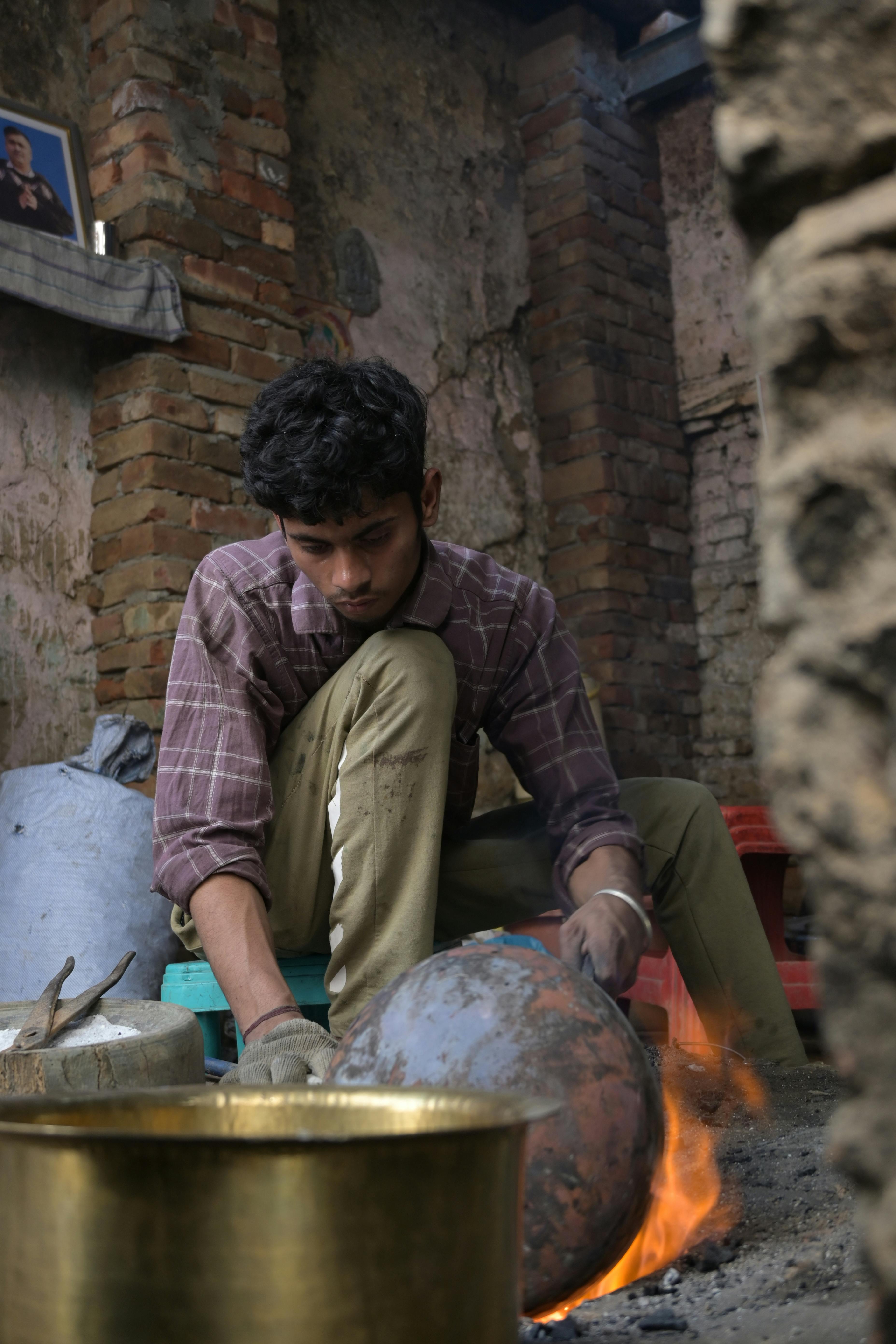 Young man working in a traditional workshop in Amritsar, India, crafting with fire and metal.