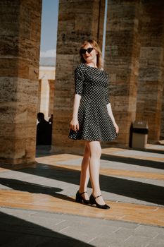 Young woman in polka dot dress and sunglasses posing outdoors. Fashion highlight of summer style.