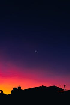 A striking silhouette against a vibrant twilight sky featuring a crescent moon at dusk.