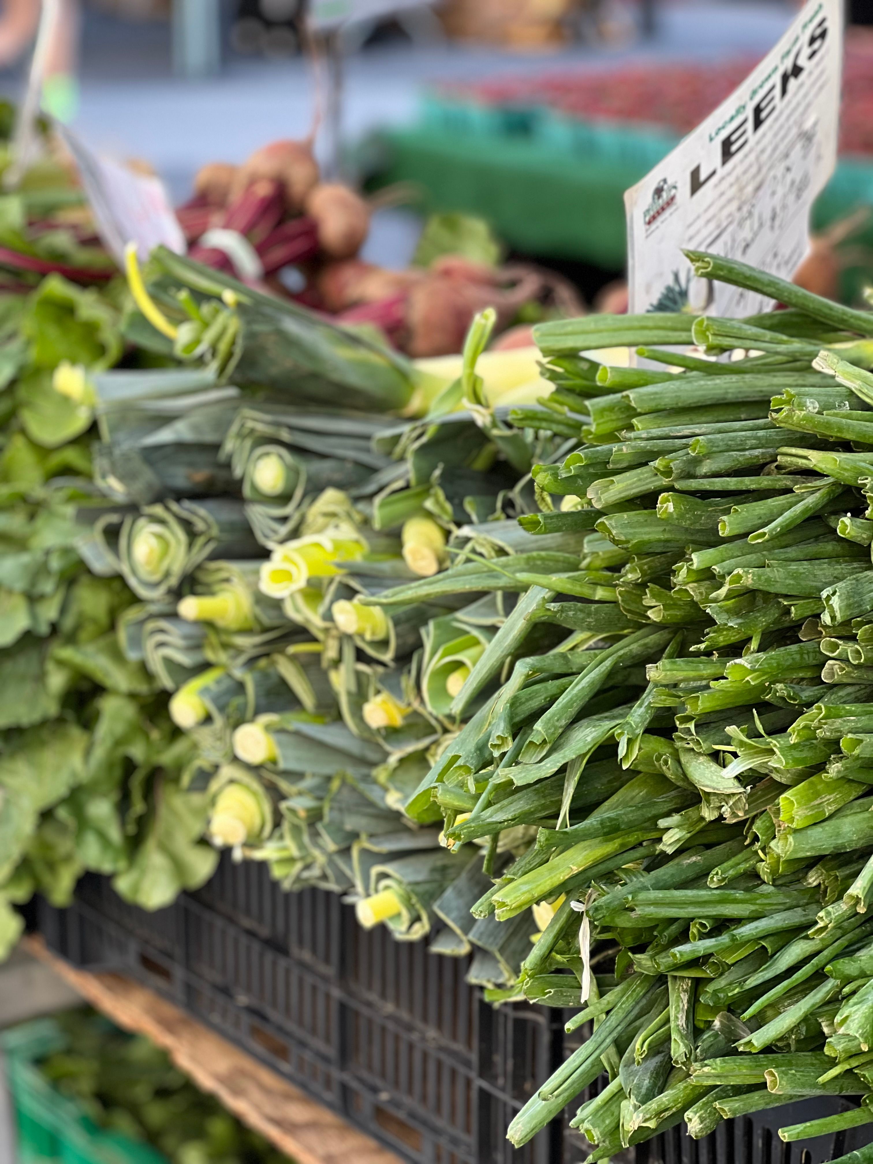 Vibrant display of fresh leeks and greens at an outdoor farmer's market stand.. vibrant, display, fresh