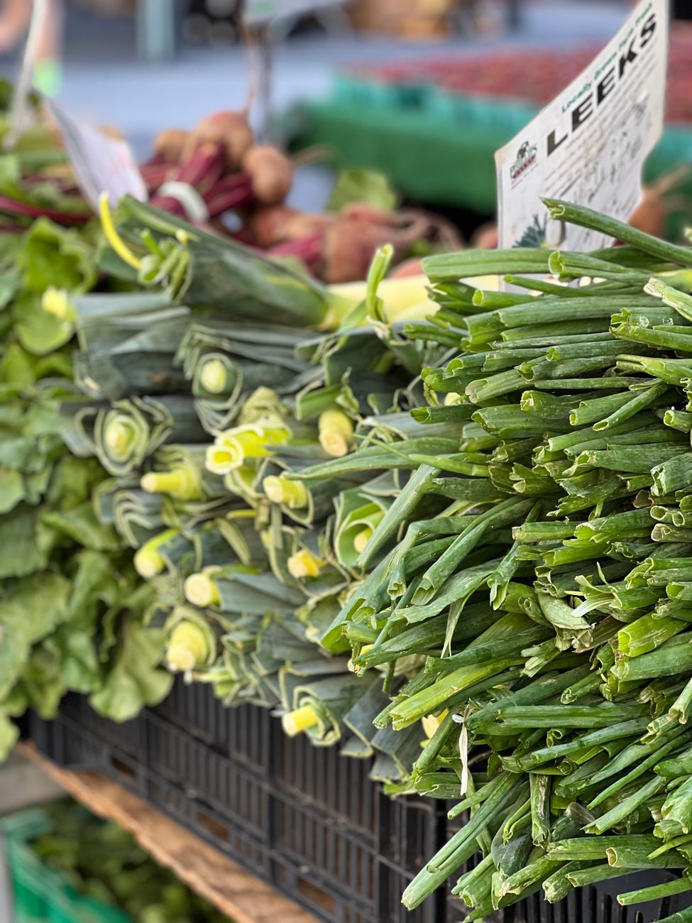 Vibrant display of fresh leeks and greens at an outdoor farmer's market stand.. vibrant, display, fresh
