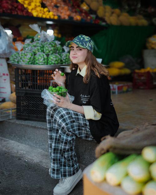 Free Young woman enjoying fresh green produce while sitting at an outdoor market display. Stock Photo