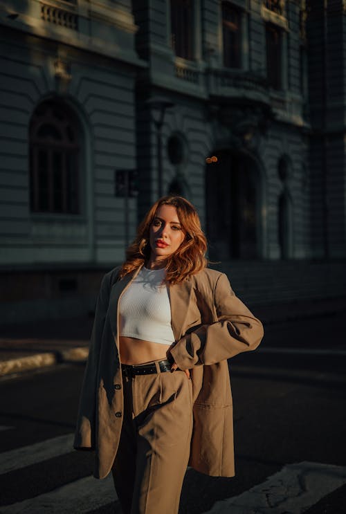 A woman in a beige suit and crop top posing on the street
