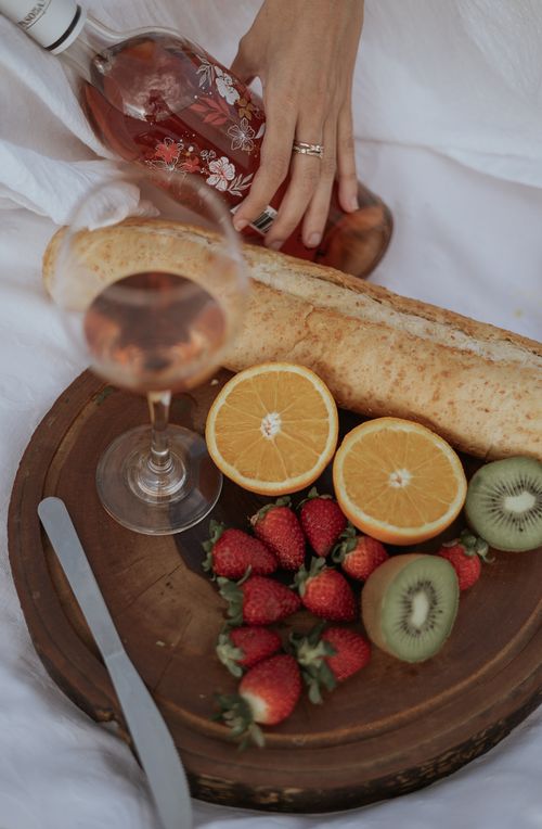 Free A sophisticated picnic setup featuring wine, bread, and fresh fruit on a wooden tray. Stock Photo