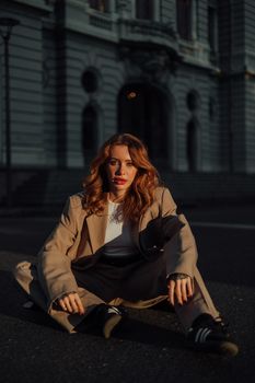 Woman sitting in urban setting wearing stylish beige coat during sunset.