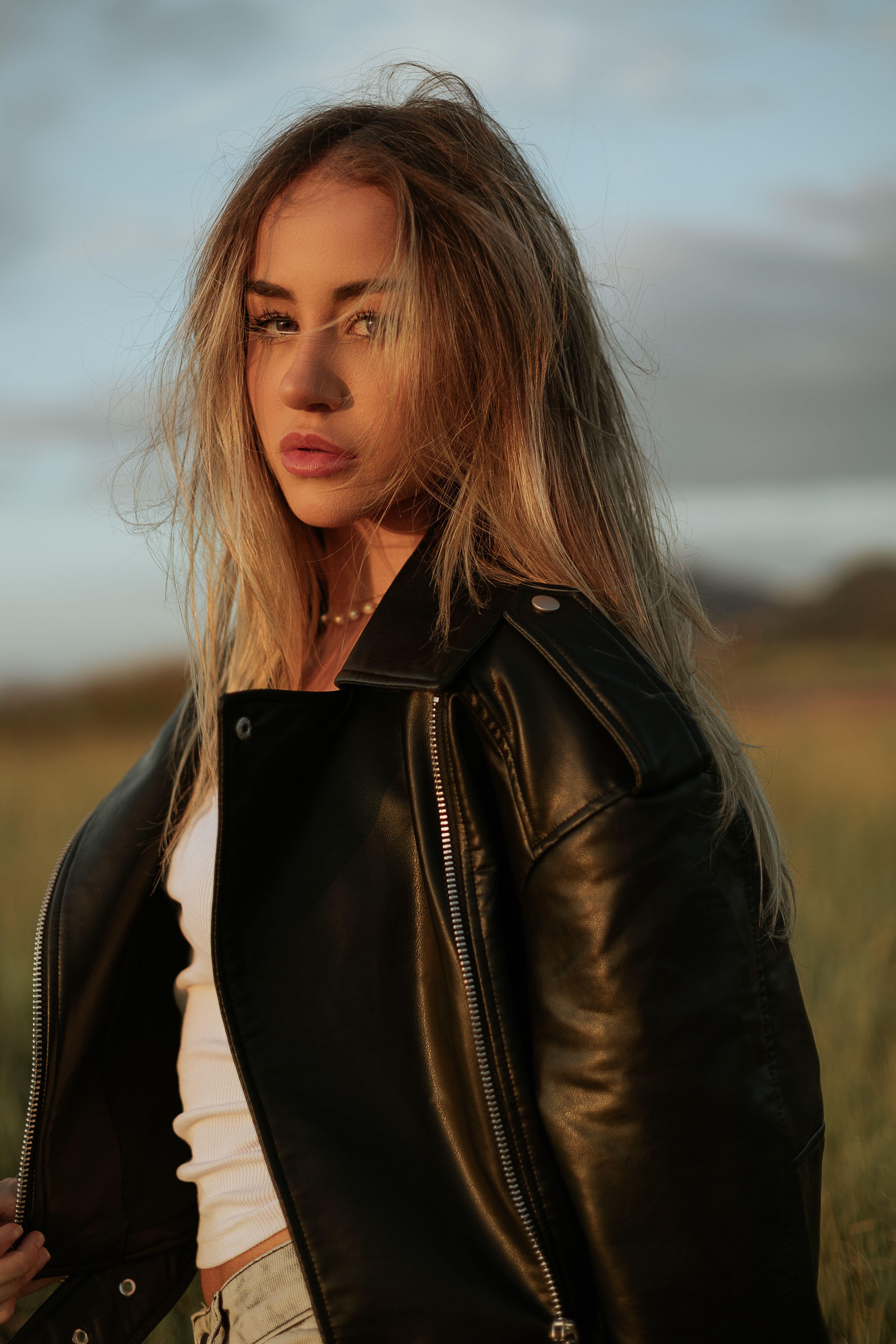 Portrait of a young woman in a black leather jacket in a meadow during sunset.
