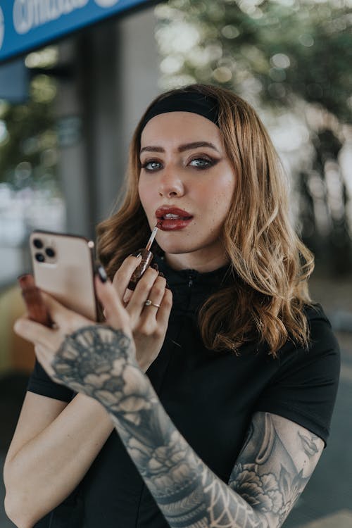 A woman with tattoos and a black shirt is looking at her phone