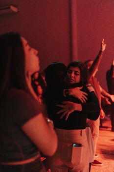 Two women embrace passionately in a dimly lit nightclub, red lights casting a warm mood.