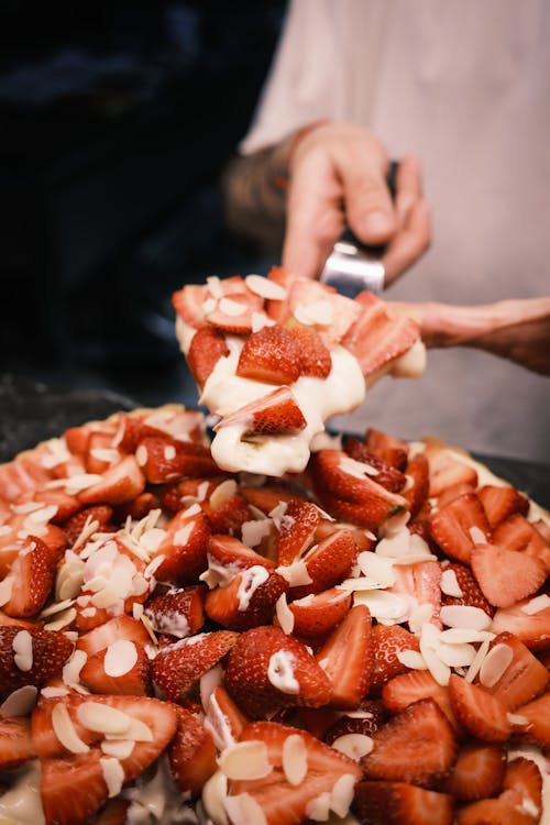 A person cutting strawberries and almonds on a pizza