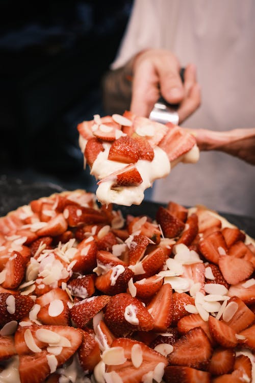 A person cutting up a pizza with strawberries