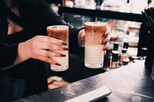 Close-up of a barista's hands holding two iced coffees on a café counter.