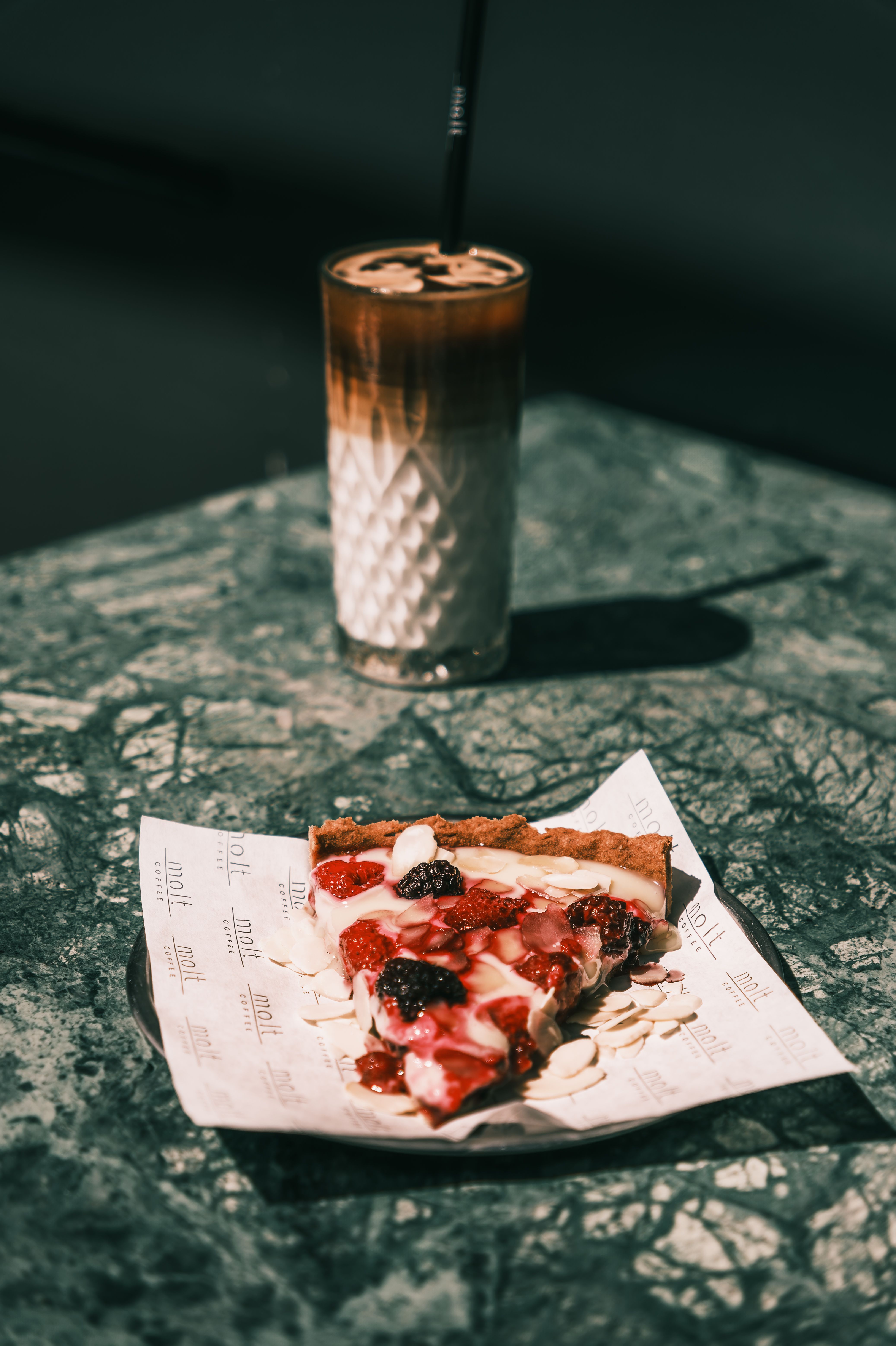 A close-up of a berry tart and iced coffee on a textured marble table, perfect for food enthusiasts.