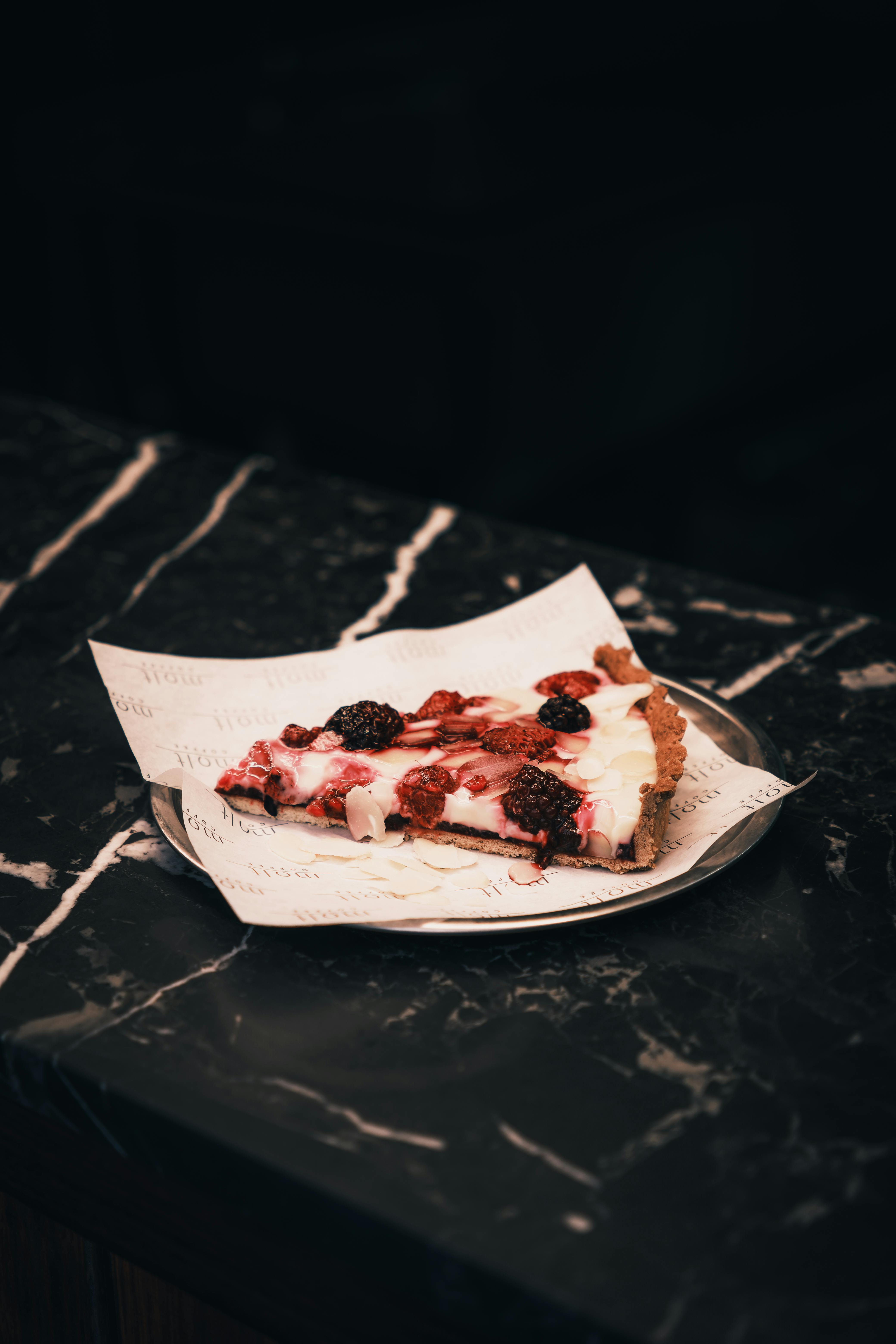 A scrumptious slice of berry tart with creamy topping on a marble table, perfect dessert treat.