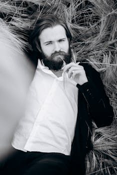 一位穿着西装的胡须男人躺在田野里，他的单色肖像传达出轻松而严肃的氛围