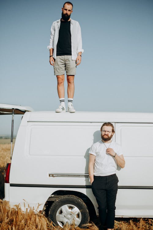 Photo of a Man Standing on Top of White Van and a Man Standing Beside the Van