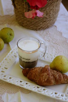 Enjoy a cozy breakfast with coffee, croissant, and pears on a lace tablecloth.