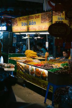 Illuminated Vietnamese food stall at a bustling night market, showcasing colorful delicacies.