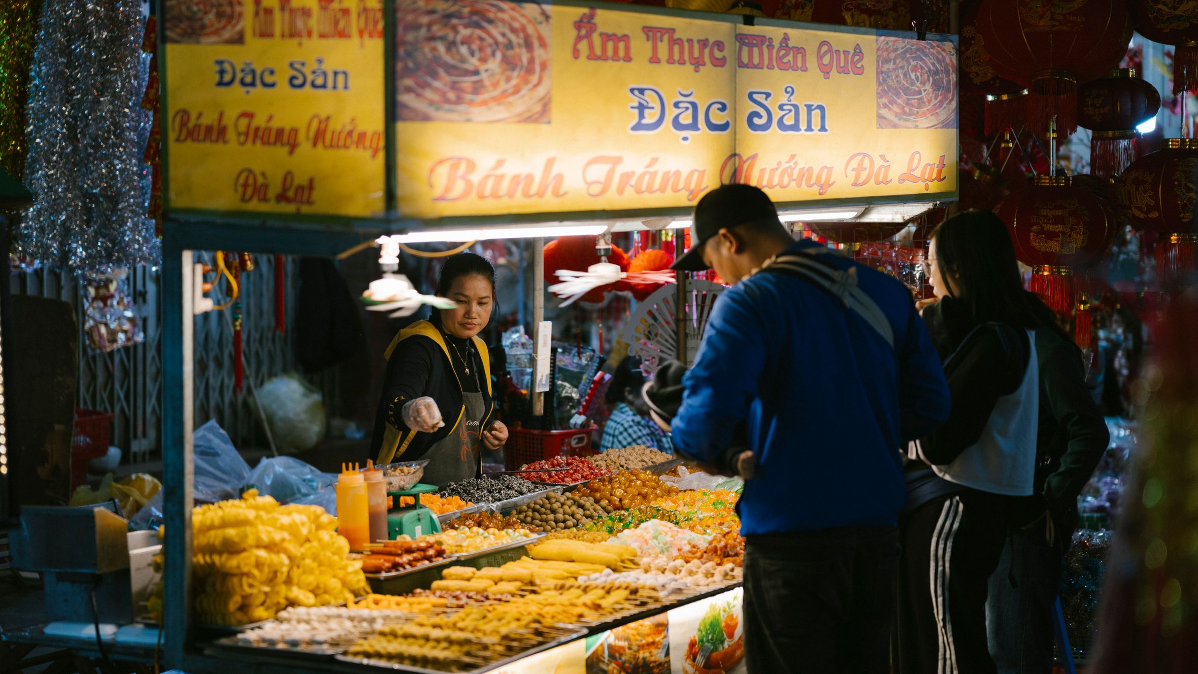 Vibrant night market scene with a Vietnamese food stall offering diverse local snacks and delicacies.