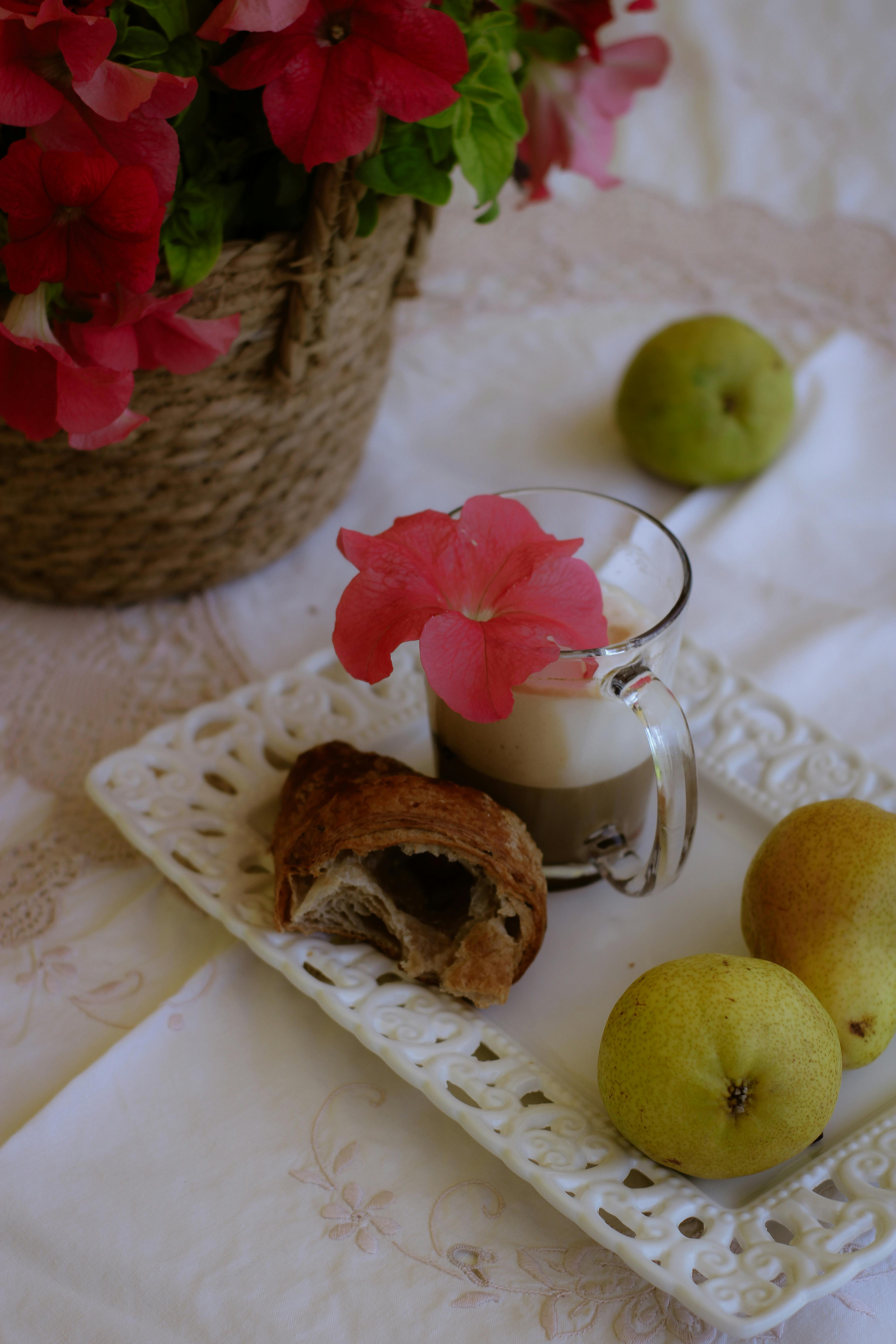 Elegantly arranged breakfast setup with coffee, croissant, pears, and vibrant flowers.