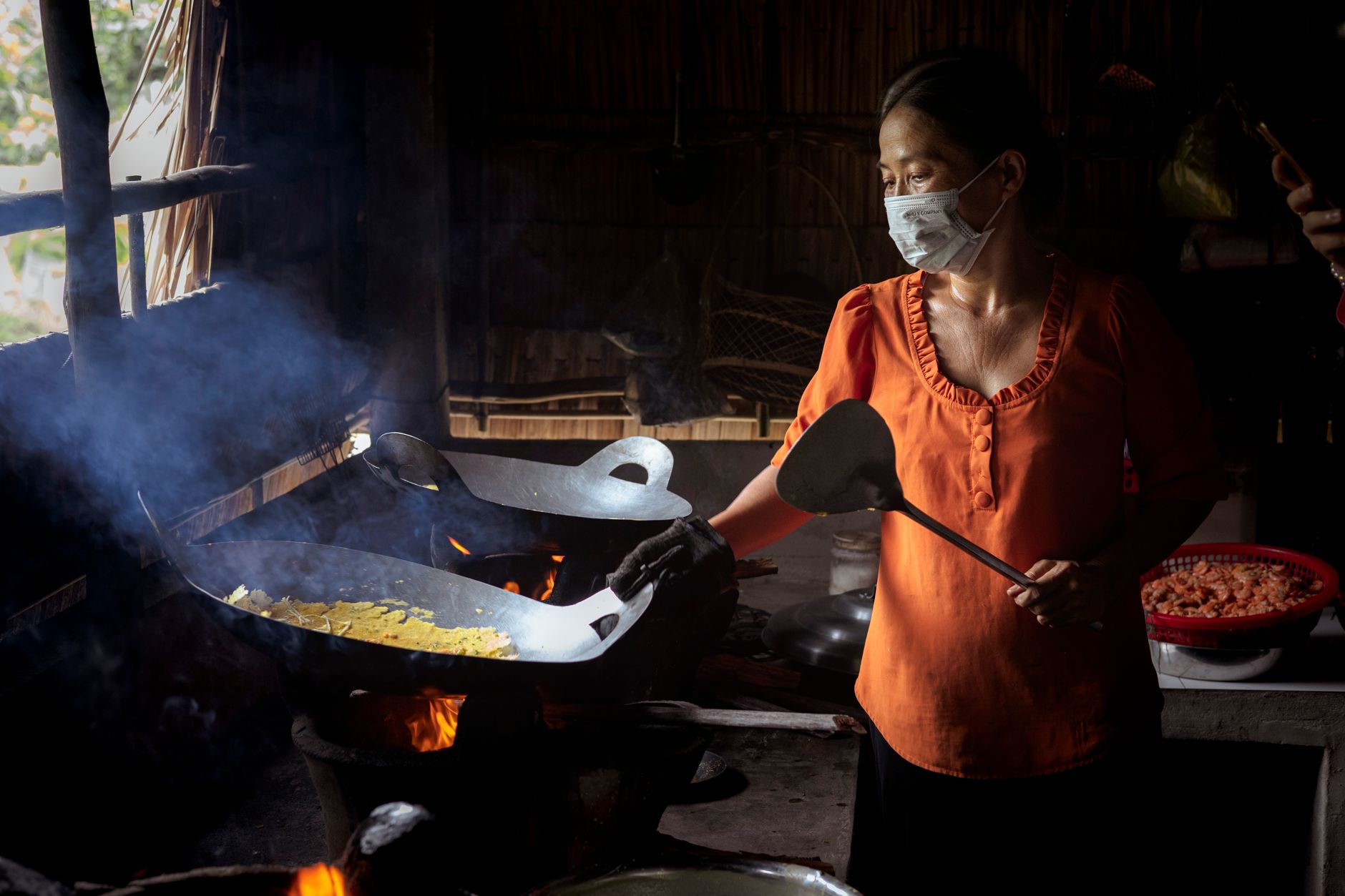 A woman wearing a face mask cooks with a wok in Trà Vinh, Vietnam, showcasing traditional methods.