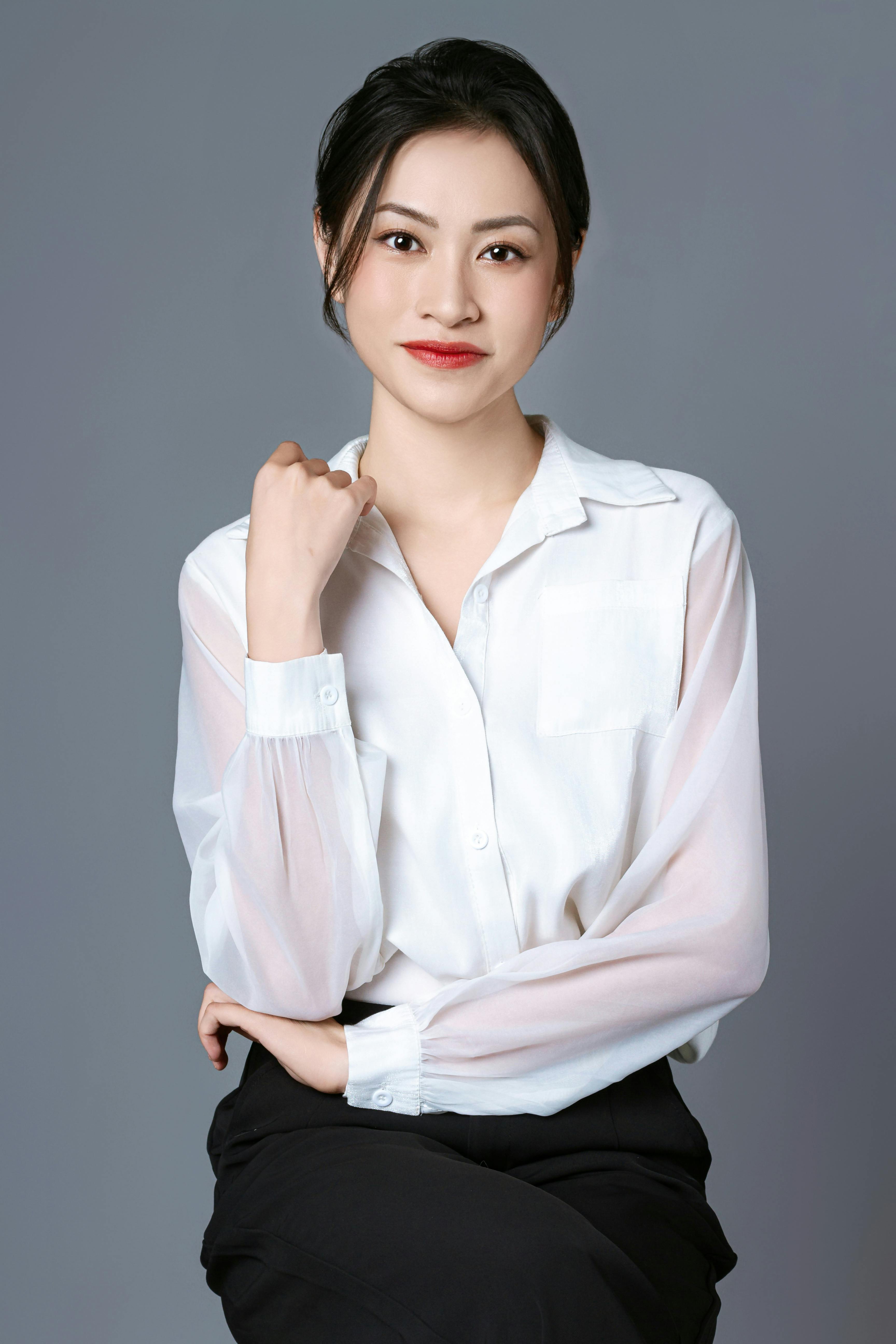 Sophisticated portrait of an Asian woman in a white shirt against a neutral background, exuding elegance and poise.