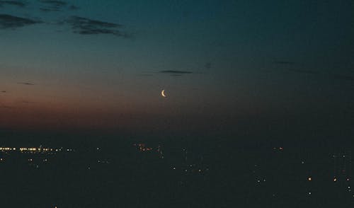 Urban Twilight Serenity: A crescent moon graces the evening sky, casting a tranquil glow over the city lights below. A perfect blend of nature's calm and urban charm. 