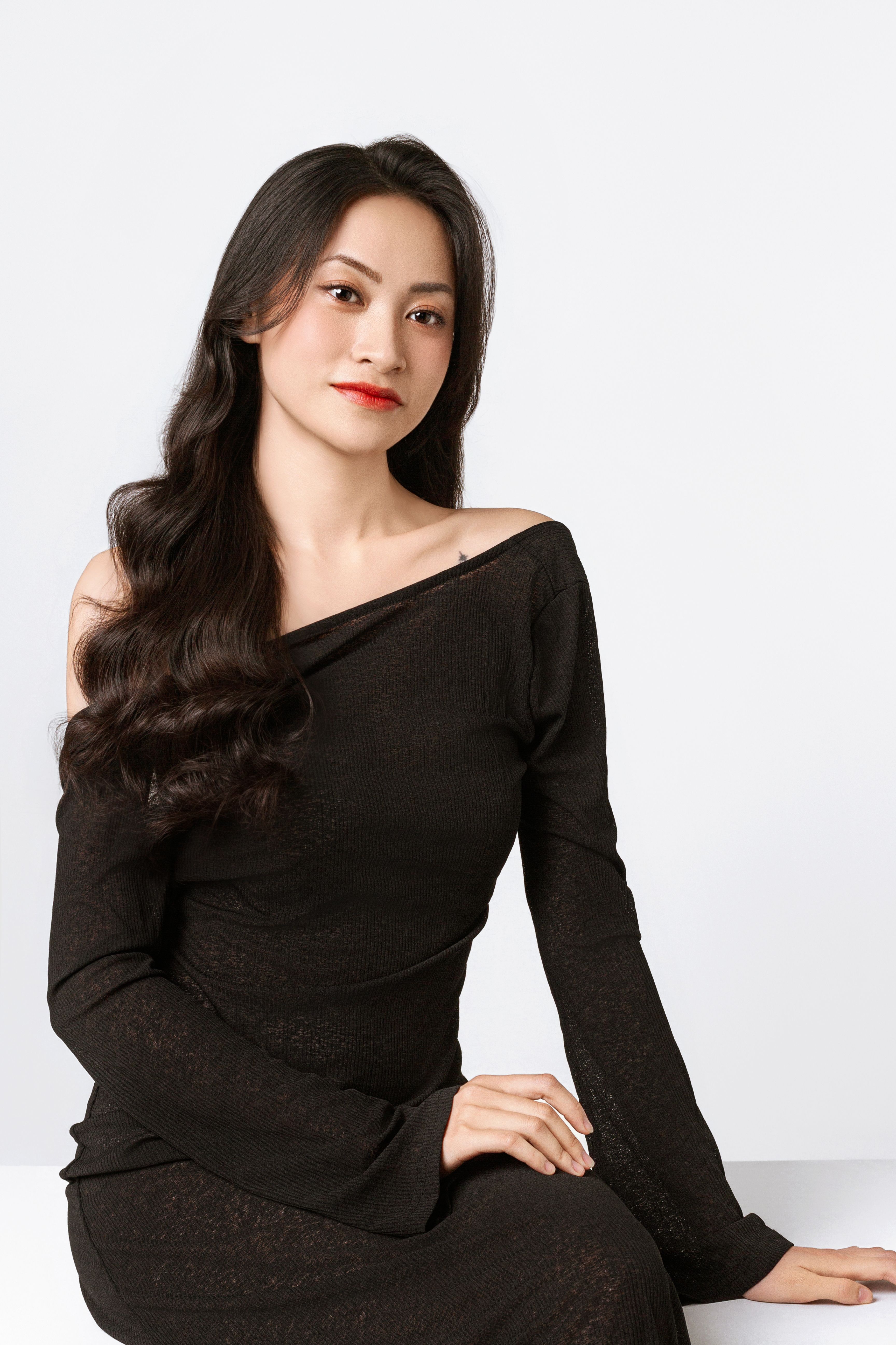 A stylish woman in a black dress poses elegantly in a minimalist studio setting.