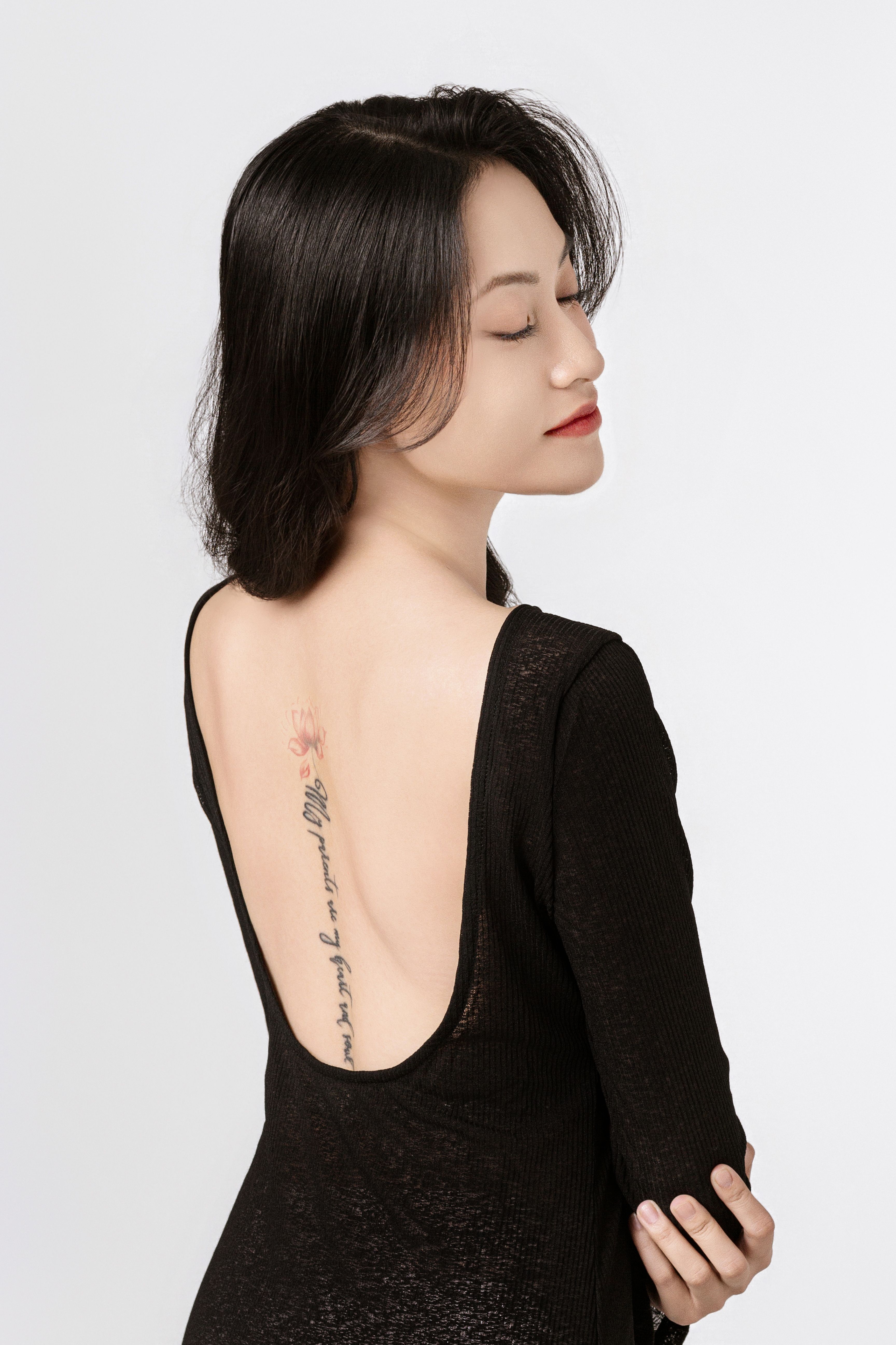 Serene woman with back tattoo and closed eyes, in a black backless dress.