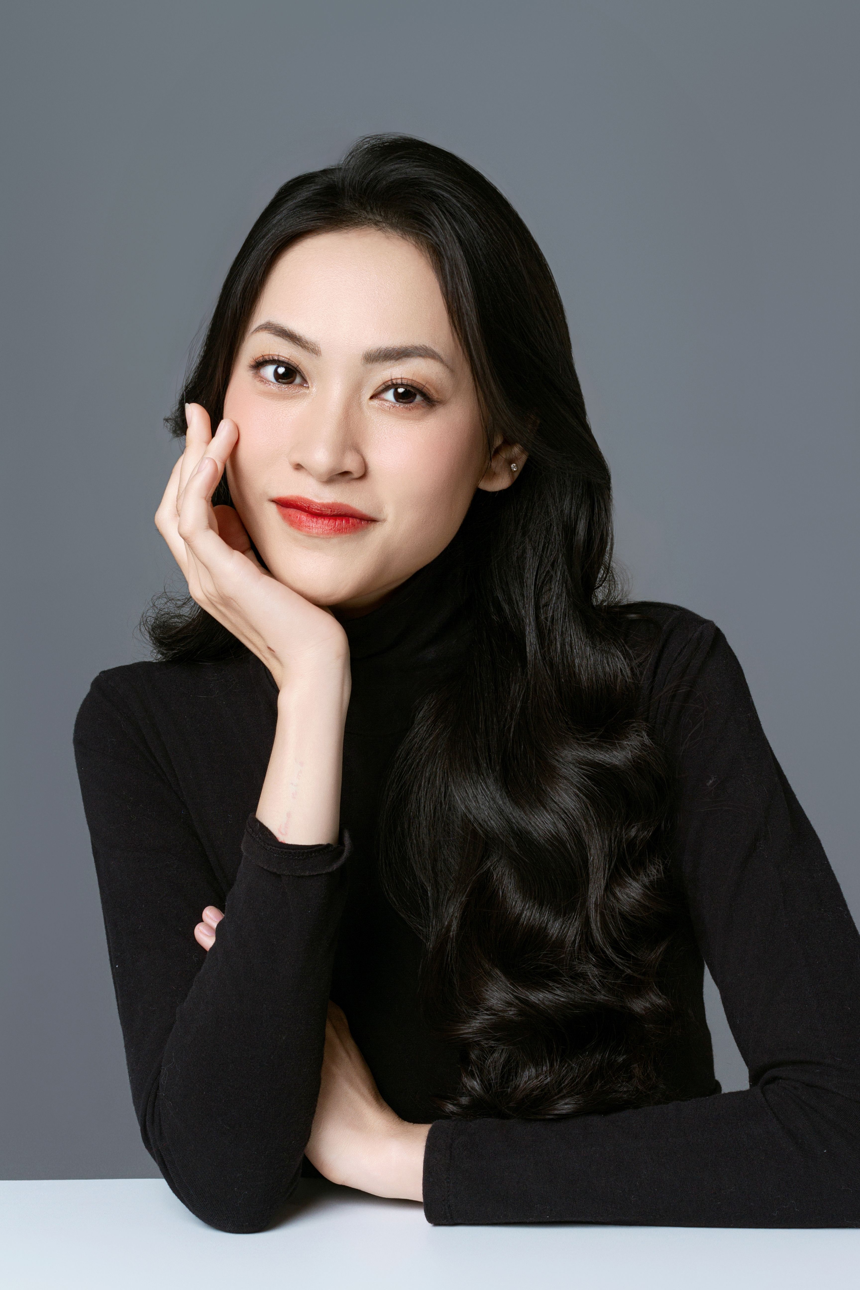 Portrait of a serene woman in a studio with a gray background, wearing a black turtleneck.