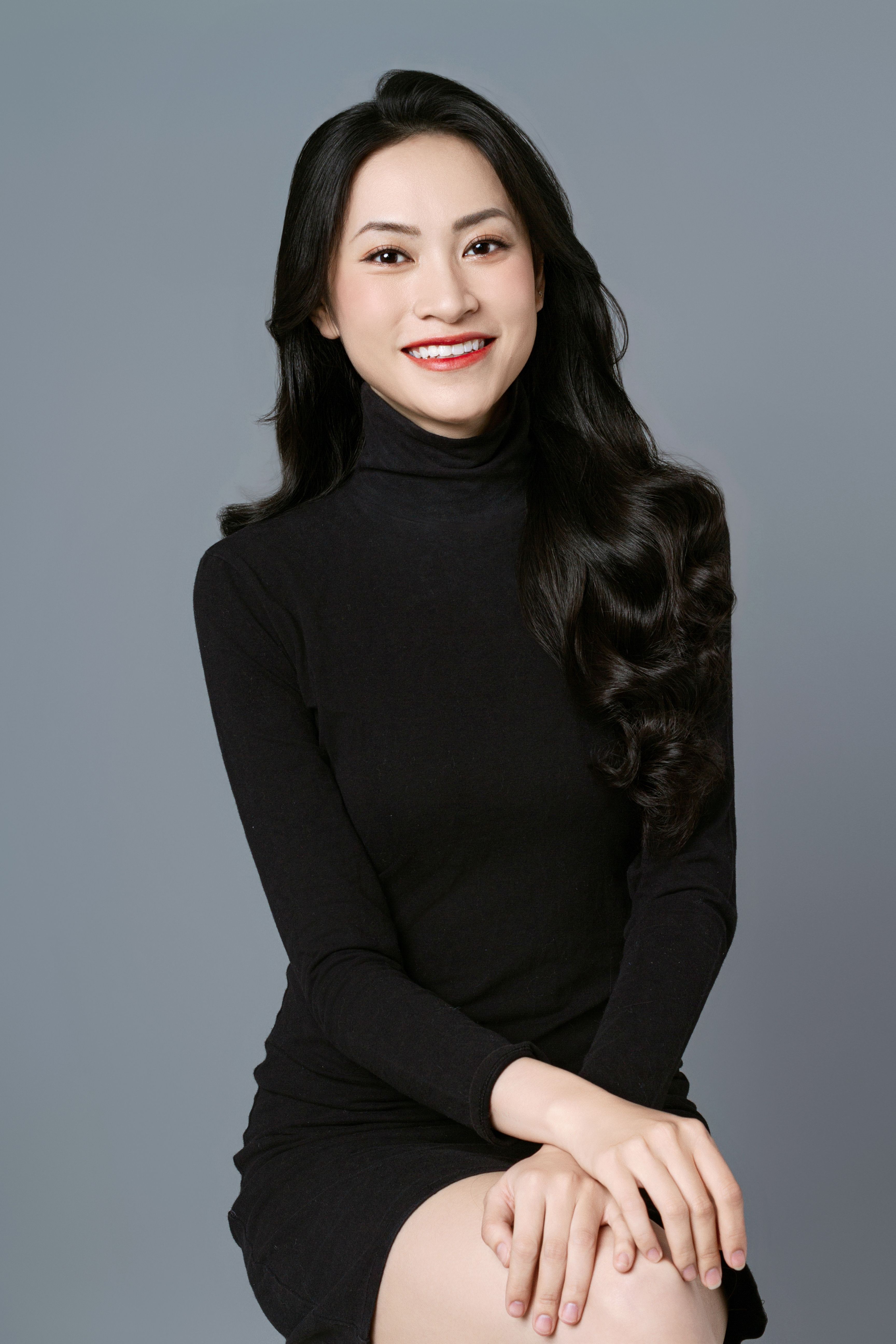 Portrait of a smiling Asian woman in a black dress, showcasing elegance and confidence in a studio setting.