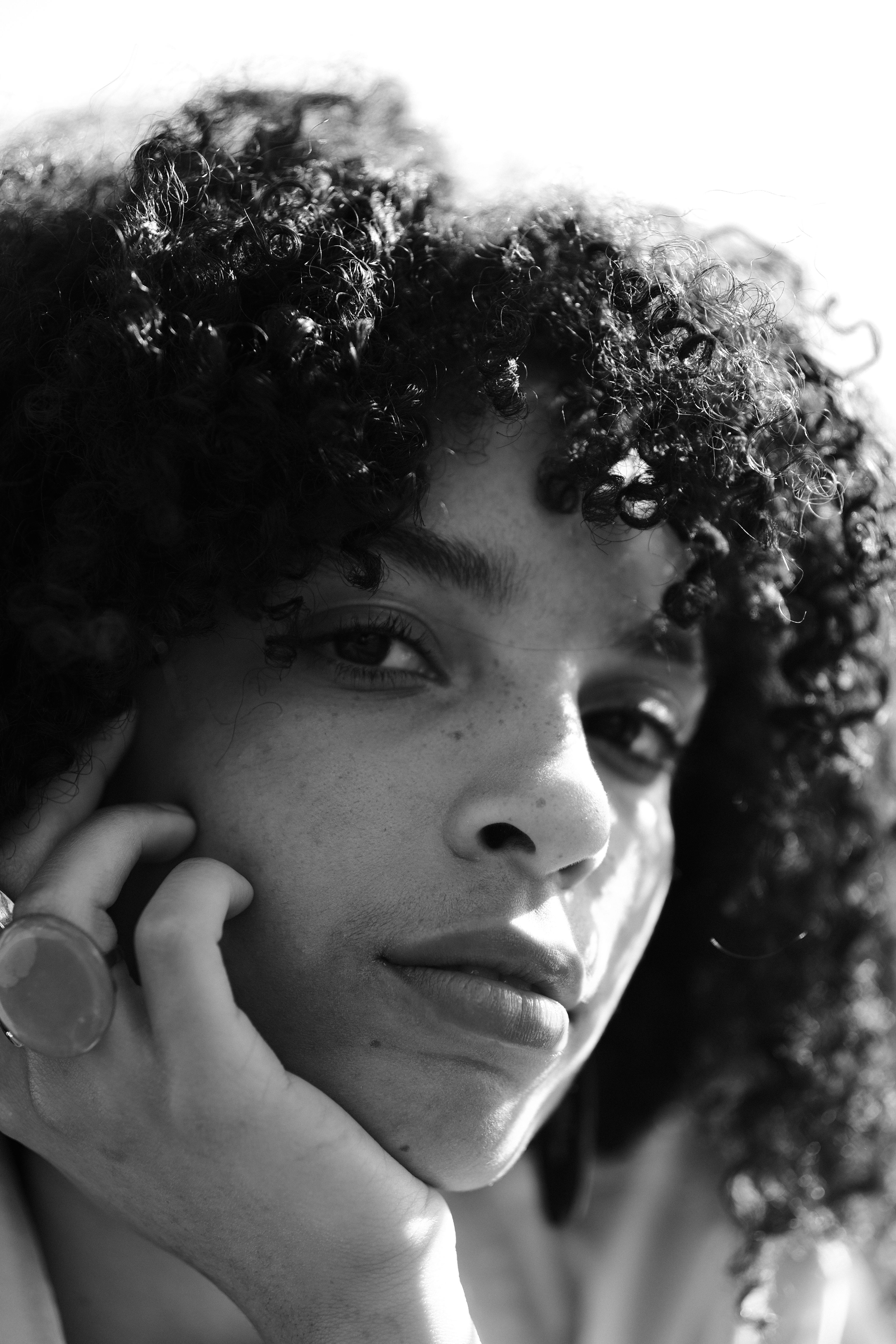 Serene black and white portrait of a young woman with curly hair, posing thoughtfully.