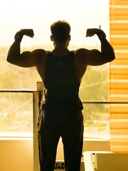 Backlit silhouette of a muscular man flexing in a gym setting, exuding strength and fitness.
